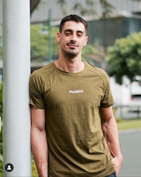 a man wearing a green t - shirt leaning against a pole