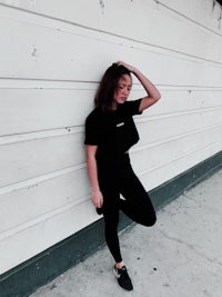a woman leaning against a wall wearing black leggings and a black crop top