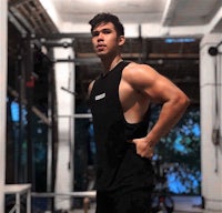 a man standing in a gym wearing a black tank top